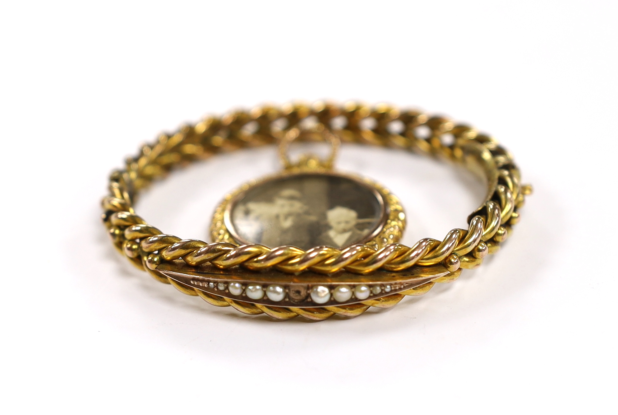 An Edwardian 9ct and graduated seed pearl set hinged bangle (pearl missing), gross weight 12.7 grams and a yellow metal overlaid locket.